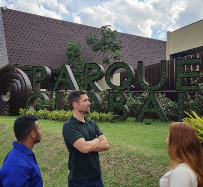 Pessoa em pé com braços cruzados e atrás o letreiro do Parque Global